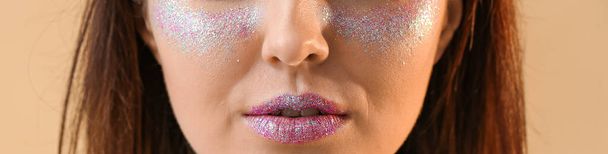 Beautiful young woman with glitters on her face against color background, closeup - Photo, Image
