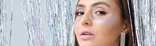 Beautiful young woman with glitters on her face against light background, closeup - Valokuva, kuva