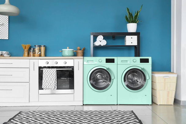 Интерьер современной кухни с двумя бирюзовыми стиральными машинами возле синей стены - Фото, изображение