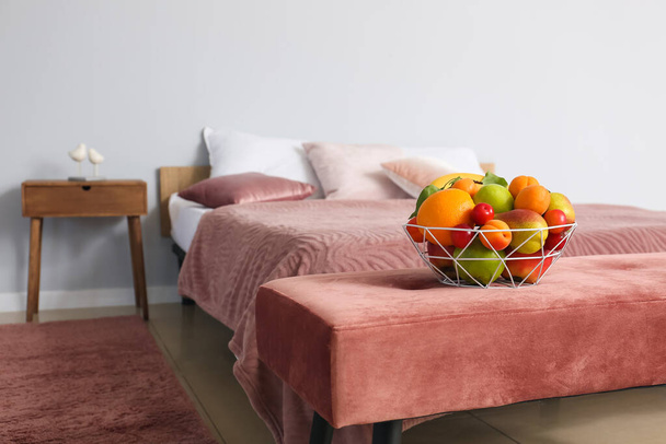 Cesta con diferentes frutas en el banco cerca de la cama en el dormitorio - Foto, imagen