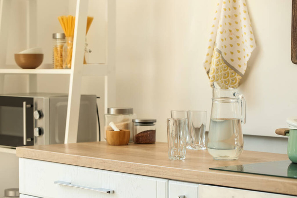 džbánek s vodou a prázdným sklem na pultu v lehké kuchyni - Fotografie, Obrázek