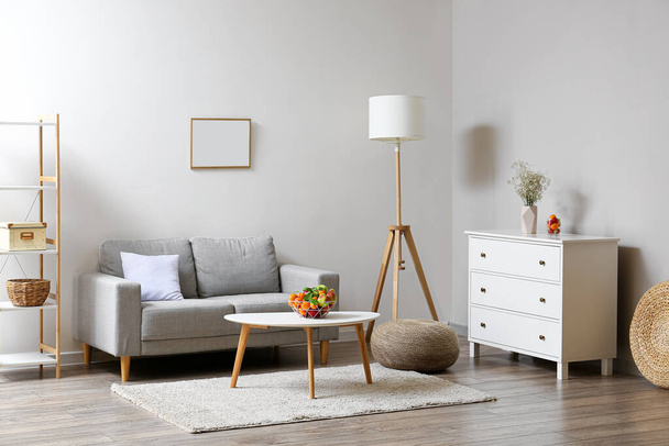 Interiér obývacího pokoje s pohovkou, truhlou zásuvek, stolní a ovocný koš u světlé stěny - Fotografie, Obrázek