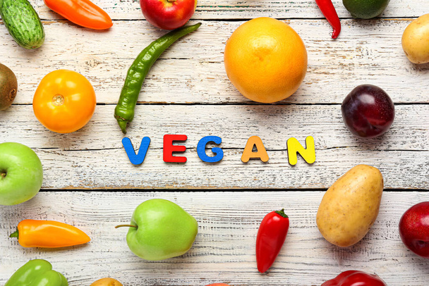 Różne owoce, warzywa i słowo VEGAN na białym drewnianym tle. Światowy Dzień Vegan koncepcja - Zdjęcie, obraz