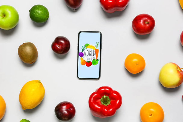 Frutta fresca, verdura e telefono cellulare con testo WORLD VEGAN DAY su sfondo grigio - Foto, immagini