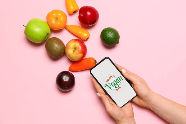 Vers fruit, groenten en vrouw met mobiele telefoon met tekst WERELD VEGAN DAG op kleur achtergrond - Foto, afbeelding