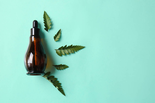 Бутылка натуральной сыворотки и листья папоротника на цветном фоне - Фото, изображение