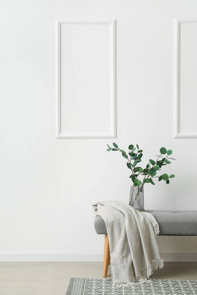 Vase with eucalyptus branches and plaid on bench near light wall - Photo, Image