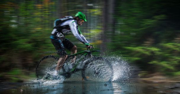 Mountain biker speeding through forest stream. - Foto, Imagem