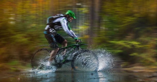 Mountain biker speeding through forest stream. - Фото, изображение