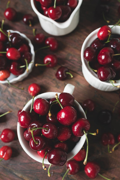 Delicious cherries in white ceramic cups on a dark wooden table - Photo, Image