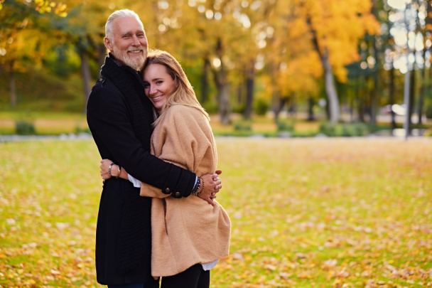 Acurrucarse hombre viejo y mujer joven al aire libre en otoño durante el día - Foto, imagen