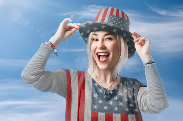Mavi gökyüzüne karşı Amerikan bayrağı giymiş mutlu genç bir kadın. ABD 'nin bağımsızlık gününü kutluyoruz. Şükran Günü. Anma Günü  - Fotoğraf, Görsel