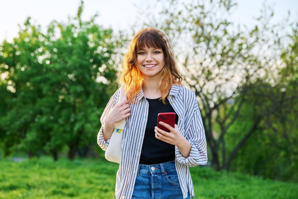 На відкритому повітрі портрет модної молодої рудої дівчини з смартфоном в руці
 - Фото, зображення