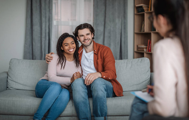 Happy millennial black woman and european guy hugs on consultation with psychologist in office interior - Photo, Image