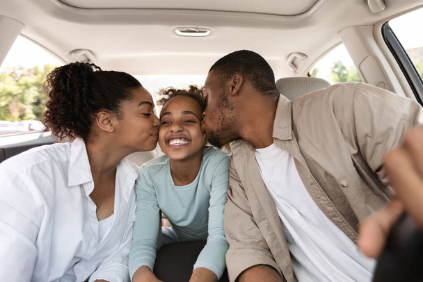 ニューカーに座っている陽気な黒人の両親のキス娘 - 写真・画像