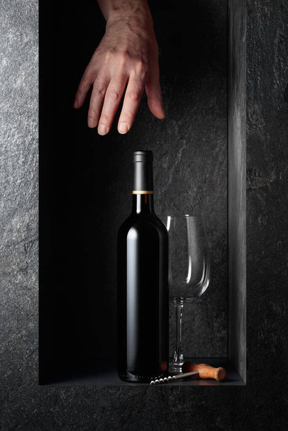 Hand reach for a bottle of red wine. A concept image on the theme of expensive wines.  - Foto, imagen
