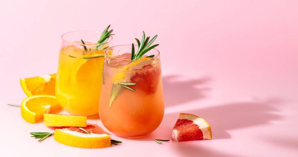 Summer cocktails with grapefruit, orange, rosemary, and ice. Drinks on pink background with copy space. Summer, tropical, fresh cocktail concept. - 写真・画像