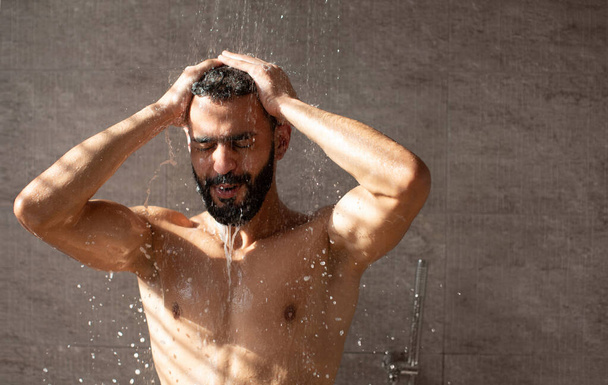 Handsome young Arabic male model taking hot shower - 写真・画像