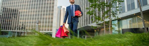 oříznutý podnikatel v obleku držet balíčky a dárkové krabice chodit mimo kancelář, nakupování - Fotografie, Obrázek