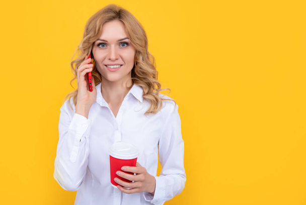fröhliche blonde Frau mit Kaffeetasse telefoniert auf gelbem Hintergrund - Foto, Bild