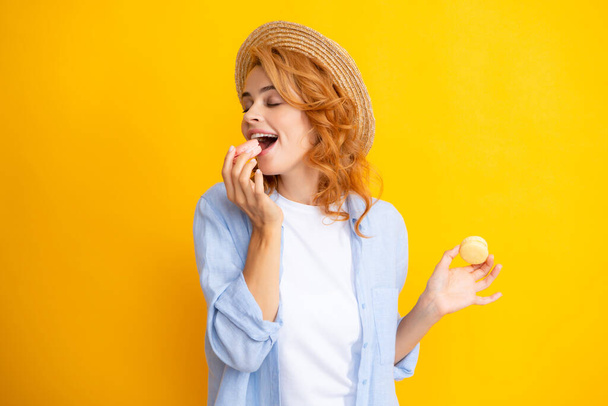 Junge zufriedene Frau auf gelbem Hintergrund, die Makronen isst. Mädchen essen französische Macarons. - Foto, Bild