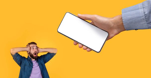 Surprised guy grabbing head looking at white empty smartphone screen - Photo, Image