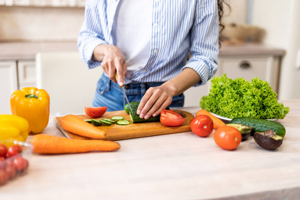 Préparation du dîner. Jeune femme coupant le concombre, cuisine plat de légumes, debout dans la cuisine à la maison, gros plan - Photo, image