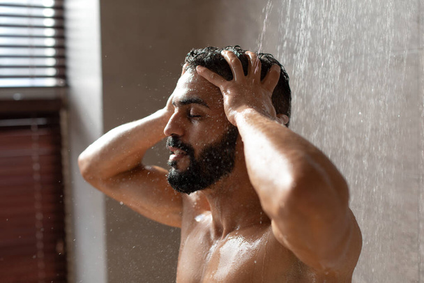 Handsome young Arabic male model taking hot shower - 写真・画像