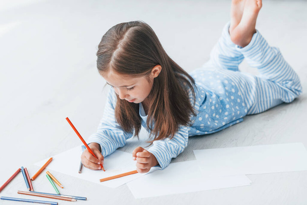Lying on the floor and drawing. Cute little girl indoors at home alone. - Foto, imagen