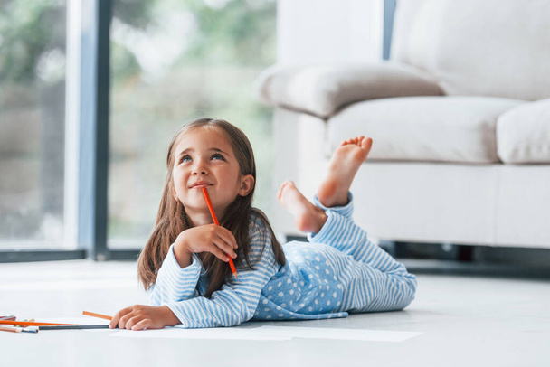 Lying on the floor and drawing. Cute little girl indoors at home alone. - Foto, afbeelding