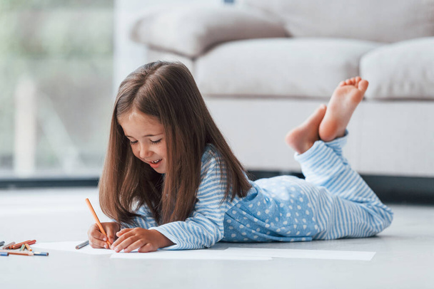 Lying on the floor and drawing. Cute little girl indoors at home alone. - Zdjęcie, obraz