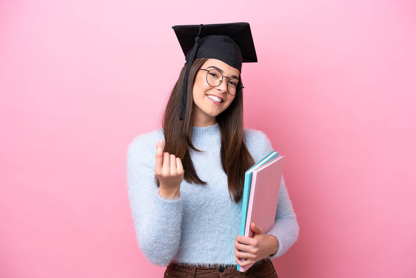 若いです学生ブラジル人女性身に着けています卒業帽子孤立ピンクの背景作りお金ジェスチャー - 写真・画像