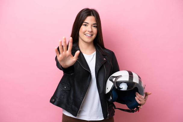 Молода бразилька з шоломом мотоцикла ізольована на рожевому фоні, рахуючи п "ять пальцями. - Фото, зображення