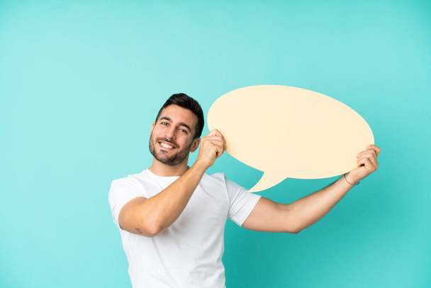 Young handsome caucasian man isolated on blue background holding an empty speech bubble - Foto, Imagem
