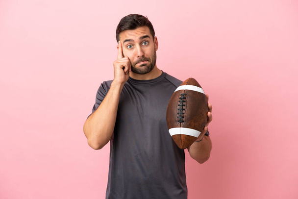 Young caucasian man playing rugby isolated on pink background thinking an idea - Fotó, kép