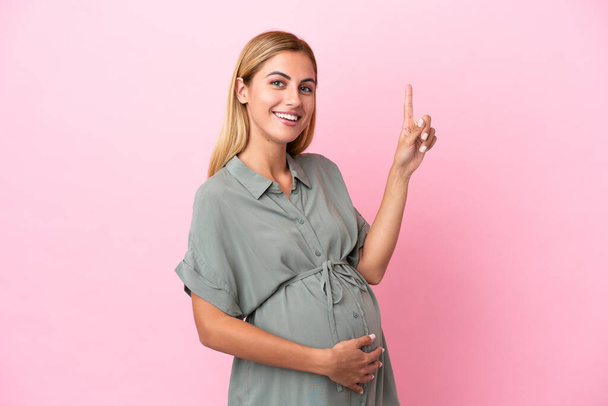 Nuori Uruguayn nainen eristetty sinisellä pohjalla raskaana ja osoittaa ylöspäin - Valokuva, kuva