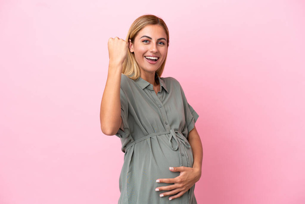 Young Uruguayan woman isolated on blue background pregnant and celebration a victory - Foto, imagen