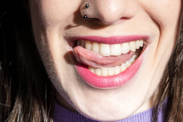 brunette nainen törröttää ulos kielensä hymyillen mustalla taustalla - Valokuva, kuva