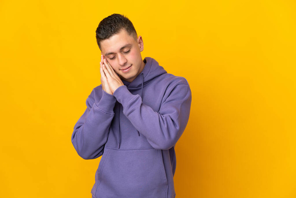 Young caucasian man isolated on yellow background making sleep gesture in dorable expression - Foto, Bild