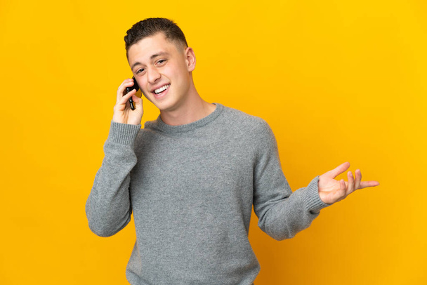 Young caucasian man isolated on yellow background keeping a conversation with the mobile phone with someone - Photo, image