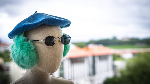 Голова манекена в шляпе, солнцезащитных очках и наушниках с городским фоном - Фото, изображение