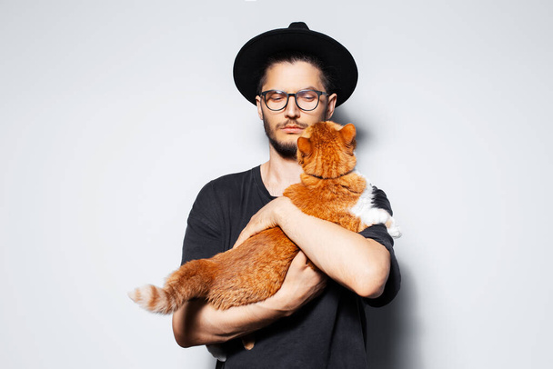 Studio πορτρέτο του νεαρού όμορφου άνδρα που κρατά μια κόκκινη γάτα. - Φωτογραφία, εικόνα