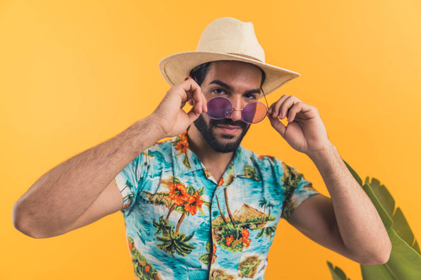 Бородатый мужчина в летней одежде надевает свои новые современные фиолетовые очки на изолированном оранжевом фоне - Фото, изображение