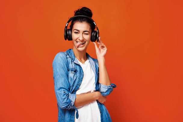 Veselá holka poslouchá hudbu. Stylový teenager těší z nové self playlist hudby přes oranžové studio pozadí. Volné místo - Fotografie, Obrázek