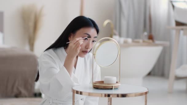 Bom dia. Jovem bela mulher asiática aplicando rímel especial para sobrancelhas, se preparando para sair - Filmagem, Vídeo