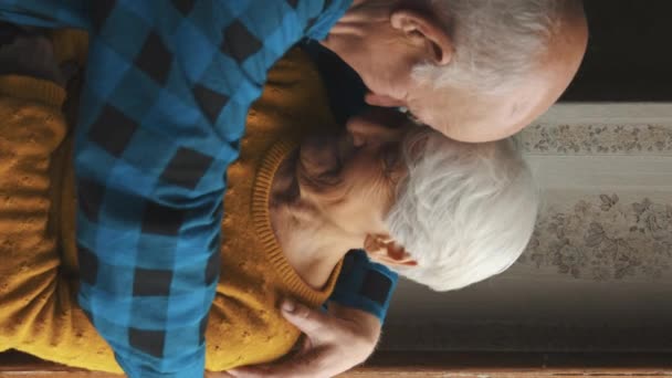 Šťastný starší pár objímání navzájem před oknem vertikální video střední záběr vnitřní láska a senioři podporují koncept - Záběry, video