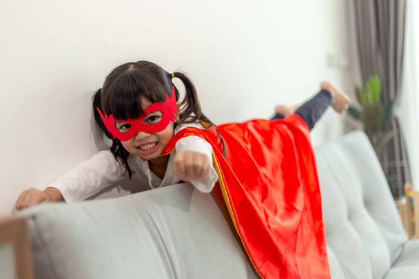 niña con un disfraz de superhéroe con máscara y capa roja en casa
 - Foto, imagen