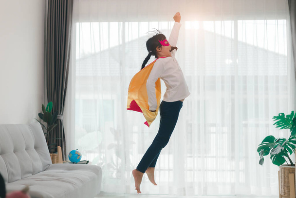 Girls child jumping on home living room couch wearing improvised superhero outfit fancy dress, playing having fun with energetic games, indoors. Discovery kids activities holiday lifestyle. - Photo, Image