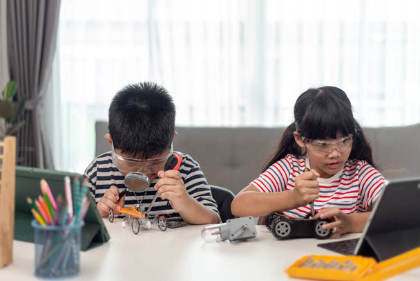 dos niños asiáticos que se divierten aprendiendo codificación juntos, aprendiendo remotamente en casa, ciencia STEM, educación en el hogar, distanciamiento social divertido, aislamiento, nuevo concepto normal - Foto, imagen