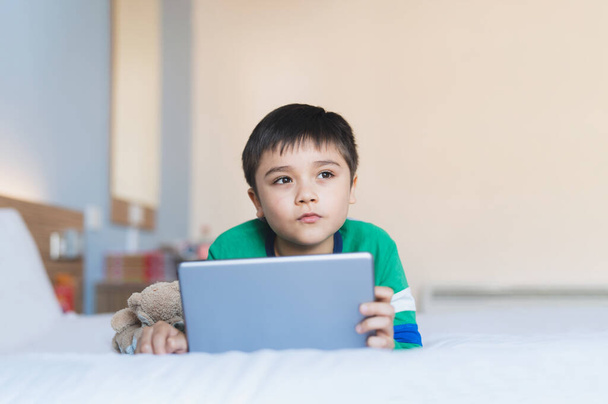 Portret Kid spelen van games online op internet in de slaapkamer, Jonge jongen met behulp van tablet typen of chatten met een vriend in de ochtend, Jeugd liggend op bed ontspannen thuis in het weekend. - Foto, afbeelding